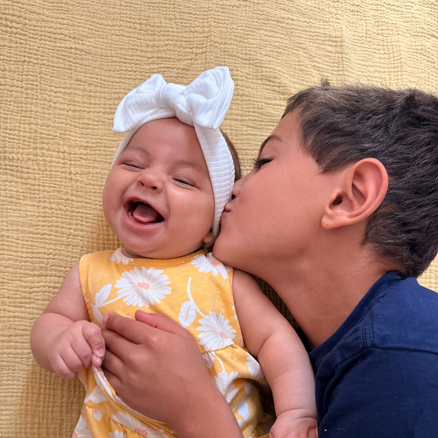 Child kissing a baby on a yellow textured blanket