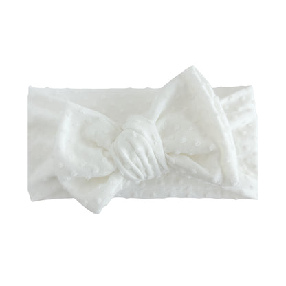 Oversized bow baby headband in white, crafted from Swiss dots knit fabric, displayed on a white background