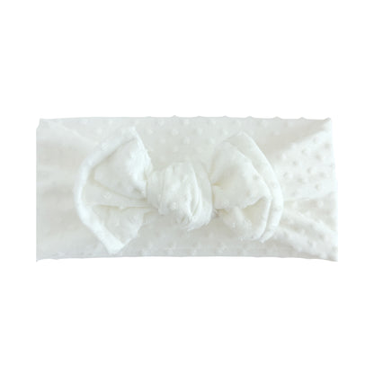 Flat lay of a white Swiss dots top knot headband with white background.