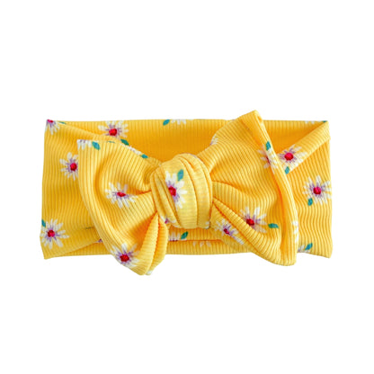 Top knot baby headband in bright yellow with white daisies print, crafted from ribbed knit fabric, displayed on a white background
