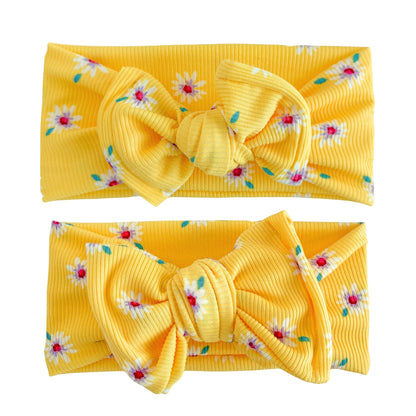 Baby girl headbands in top knot and oversized bow styles in bright yellow with white daisies print, made from ribbed knit fabric