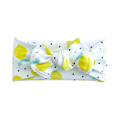 Top knot baby headband in white with yellow lemon and black tiny dot print, crafted from cotton jersey knit fabric, displayed on a white background