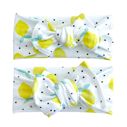Baby girl headbands in top knot and oversized bow styles in white with bright yellow lemon print, made from cotton jersey fabric